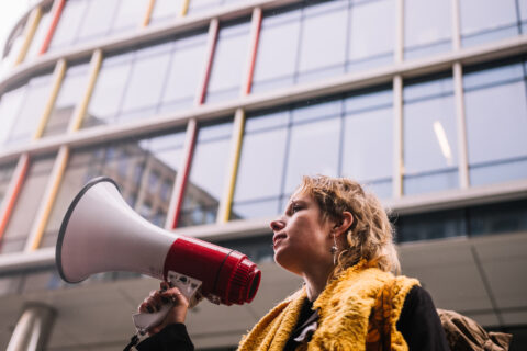 A young woman is standing in front of a building and speaking into a megaphone