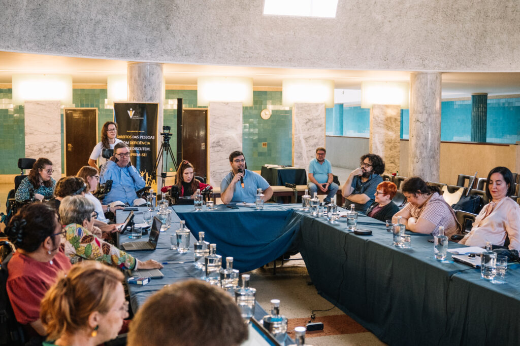 Room full of people, around twenty people around a u-shape table. Someone is speaking