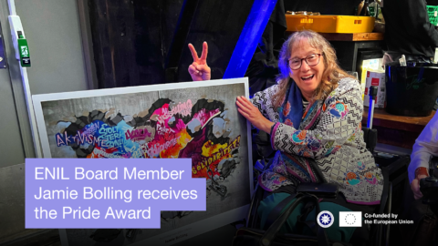 ENIL Board member Jamie Bolling receives the Pride Award. Photo of a woman in wheelchair smiling and holding a poster. ENIL logo and co-funded by the European Union