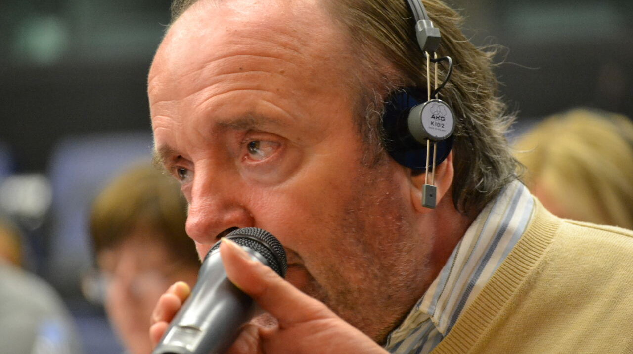 John speaking into a microphone in the European Parliament