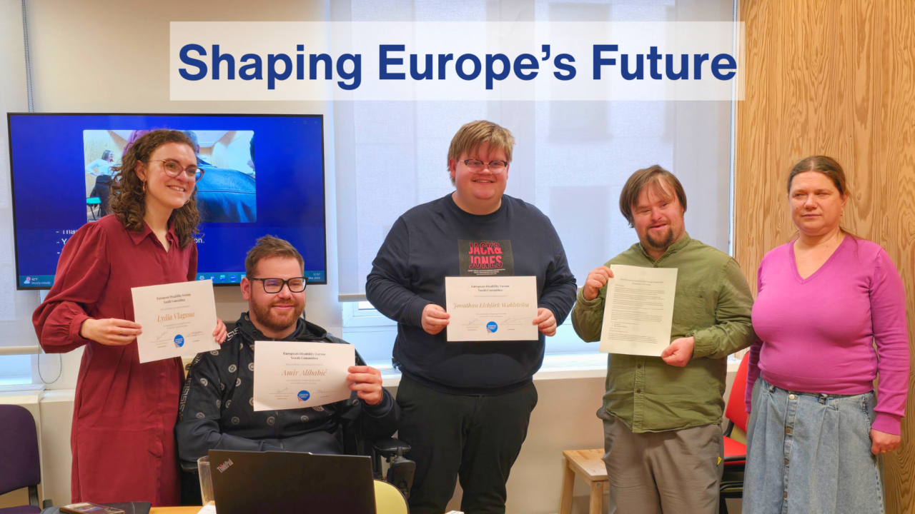 Five people stand in a meeting room holding certificates from the EDF Youth Committee, smiling after a graduation moment. A screen is visible in the background, and a banner at the top reads “Shaping Europe’s Future.”