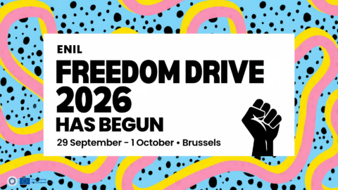 Alt text: Colourful Freedom Drive 2026 graphic with a blue background, black dots, and looping pink and yellow shapes. A large white panel reads: “ENIL Freedom Drive 2026 has begun. 29 September – 1 October • Brussels.” A raised fist symbol appears on the right, with ENIL and EU co-funding logos at the bottom left.